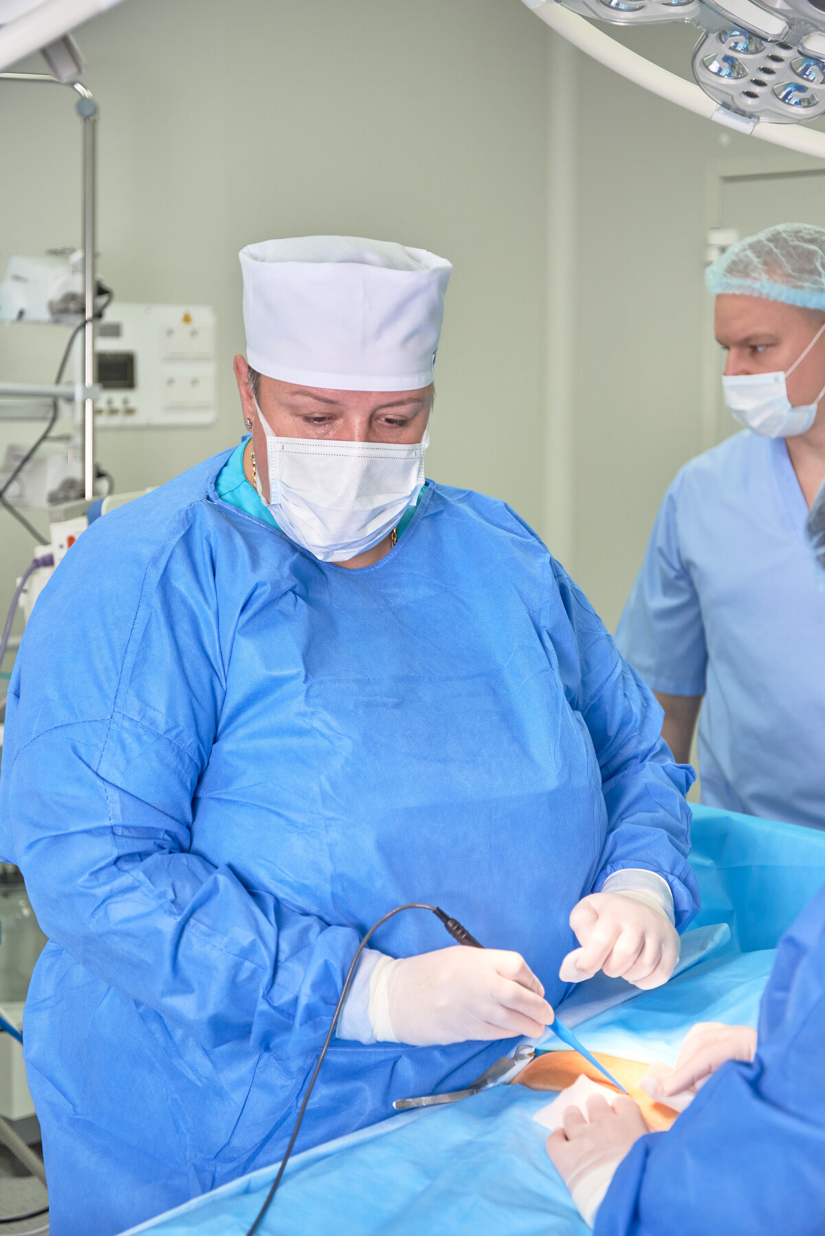 Хирурги в операционной во время полостной операции: один в синем халате и белой шапочке, другой в голубой рубашке